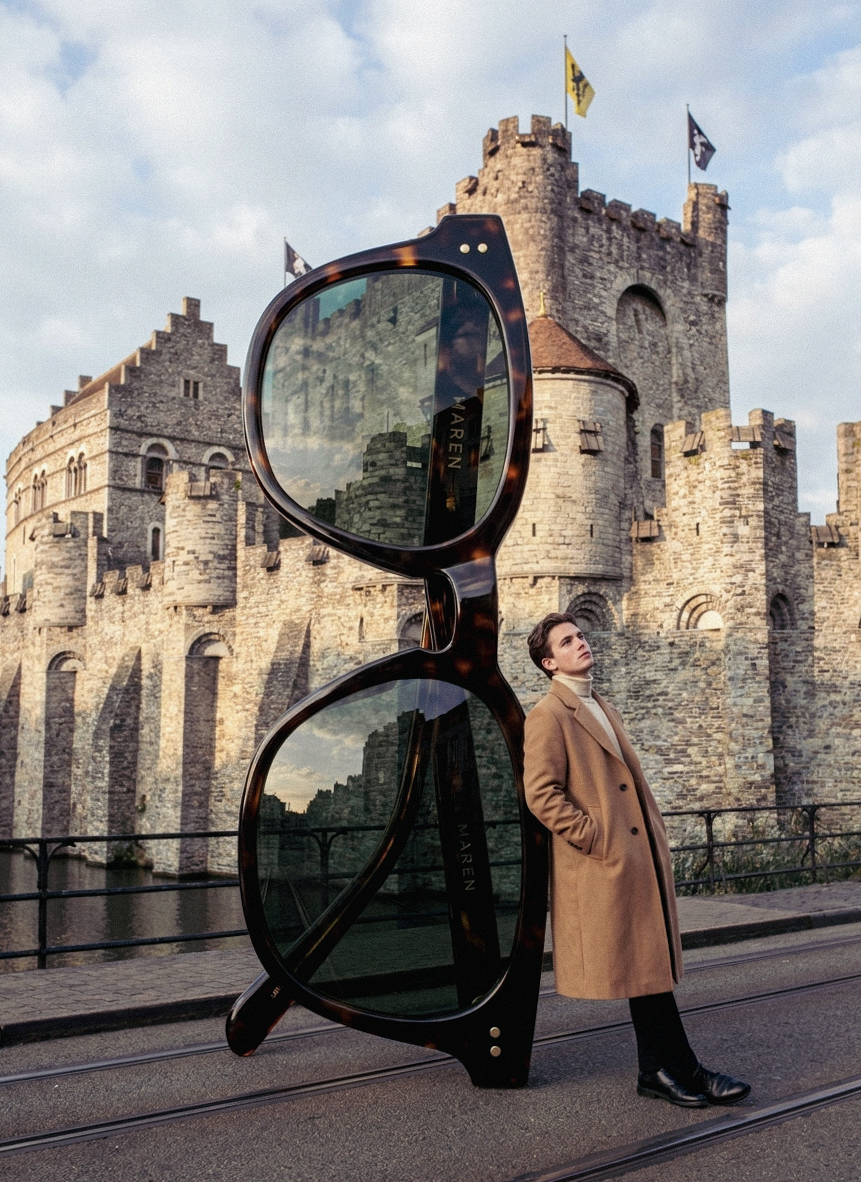 AI-gegenereerde surreële fashionvisual: een model leunt tegen een reusachtige zonnebril voor het Gravensteen in Gent